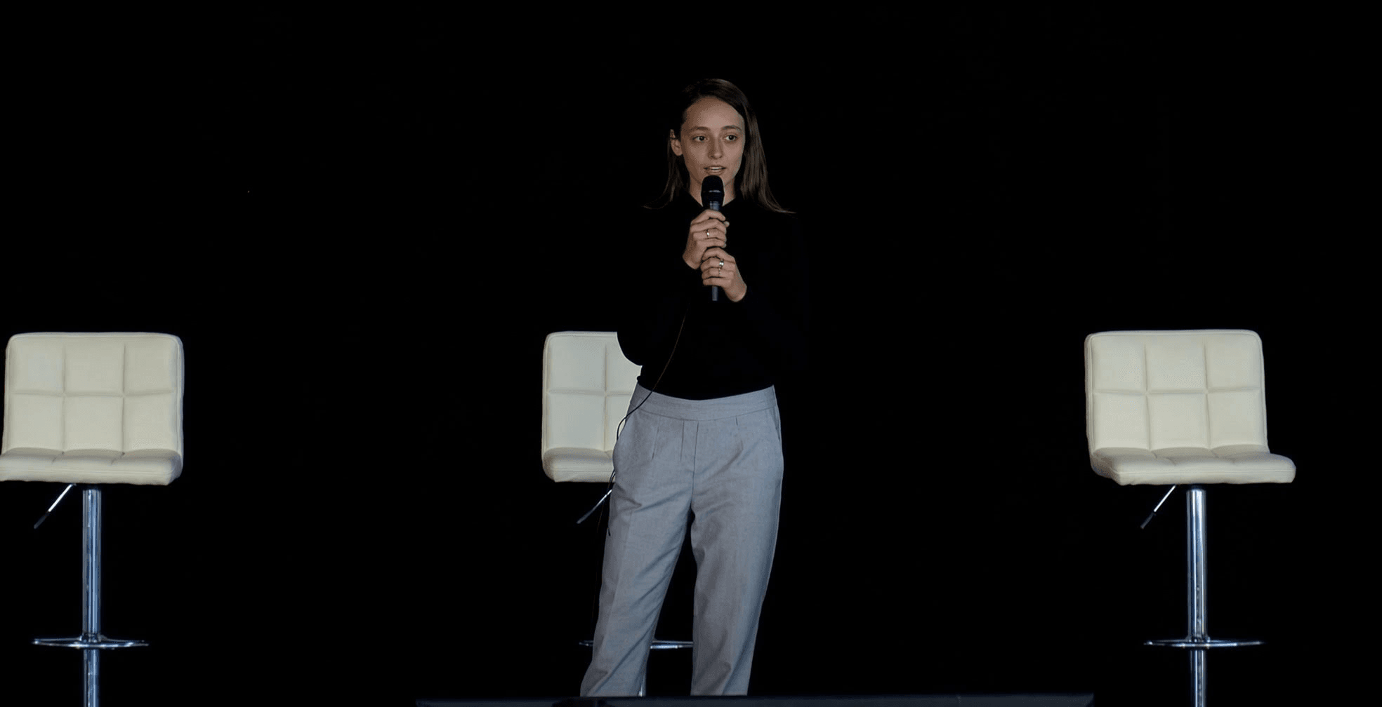 Siena Carroll speaking on stage with a handheld microphone